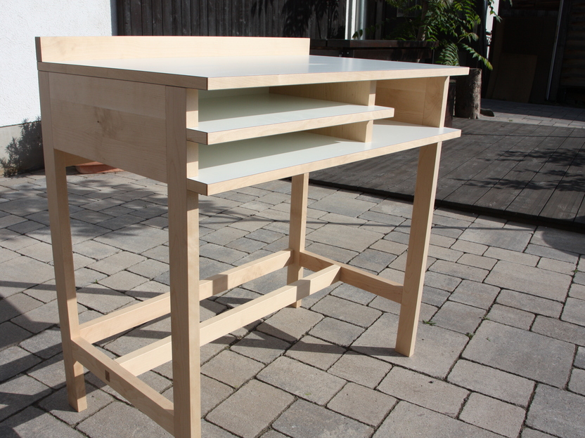 Ein ma&szlig;gefertigter Schreibtisch aus hellem Holz, der zwei offene Ablagen unter der Tischplatte bietet. Ideal f&uuml;r organisiertes Arbeiten und individuelle Anpassungen.