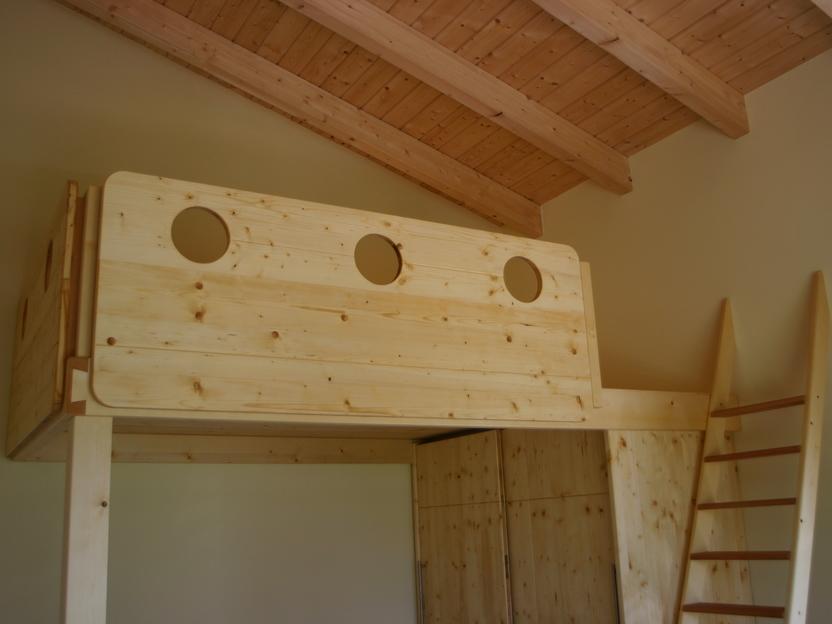 Ein Fichtenholz-Hochbett mit runden Aussparungen und einer Leiter, unter einer Dachschräge.