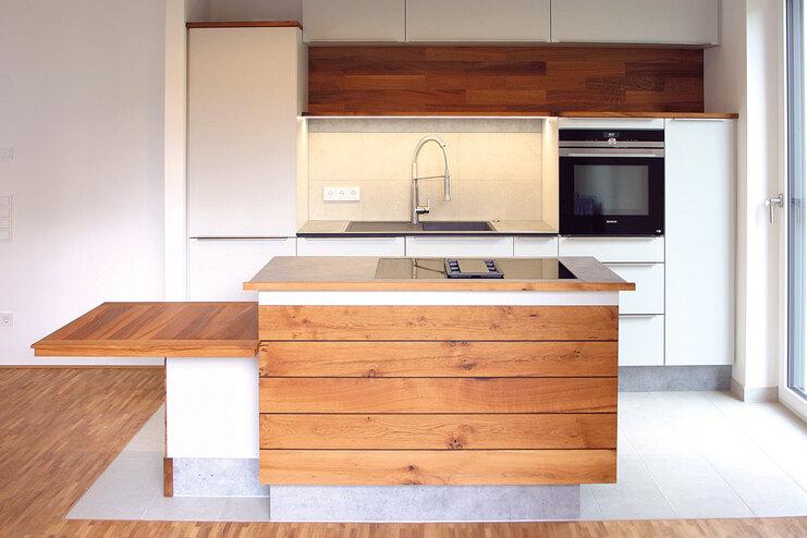 Moderne Küche mit Holzelementen und integrierter Essplatz. Helle Küche mit Holzschränken, zentraler Kochinsel und ausziehbarem Tisch.