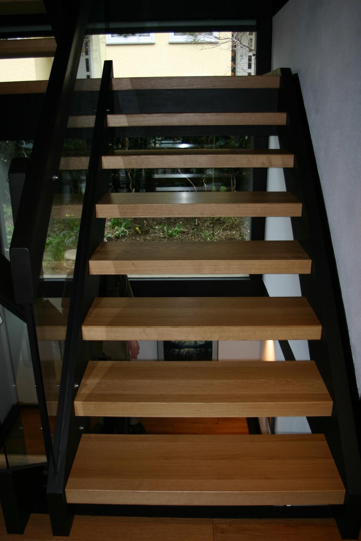 Blick auf eine Treppe mit Holzstufen und schwarzen Metallträgern in einem Haus.