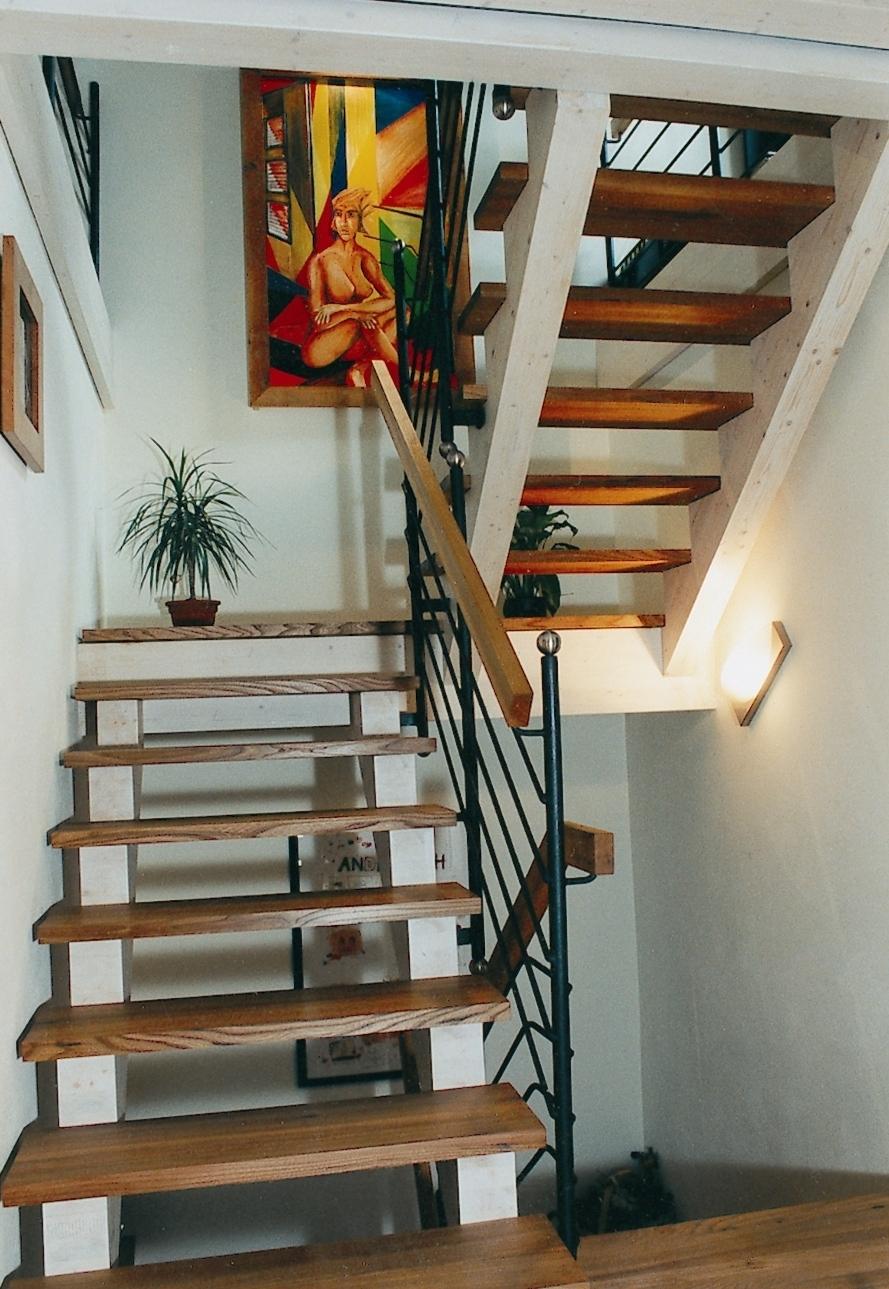 Hölzerne Treppenstufen mit weißen Wangen und schmiedeeisernem Geländer neben einem farbenfrohen Wandbild.