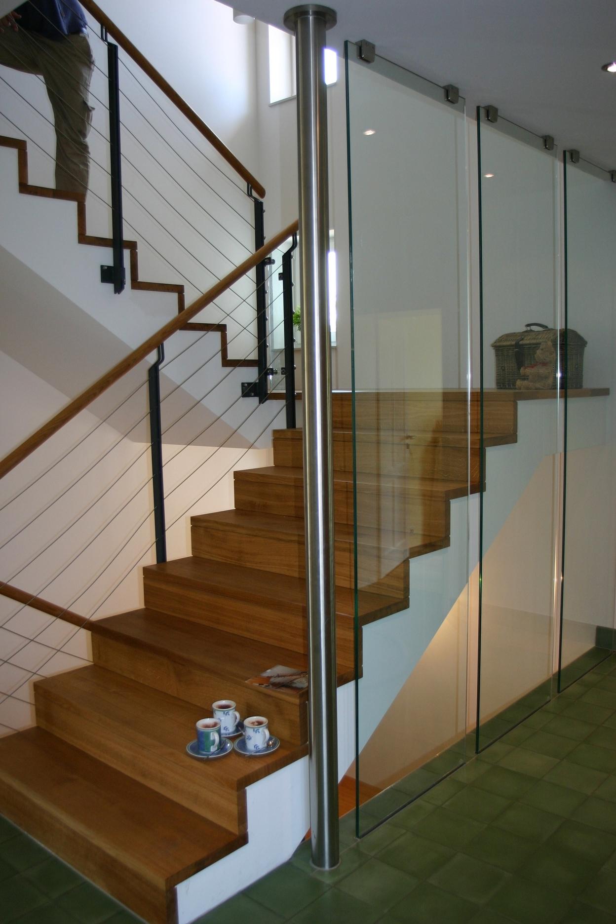 Treppe mit Eichenstufen, Glaswand auf der einen und Metallgeländer auf der anderen Seite.