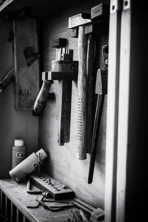 Verschiedene Handwerkzeuge aufgehängt an einer Werkzeugwand, darunter Hämmer und Meißel.