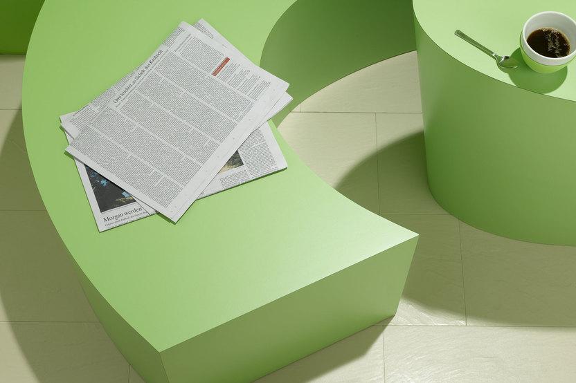 Detailaufnahme einer grünen Sitzbank mit Papierdokumenten und Tischausschnitt mit Kaffeetasse
