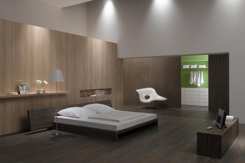 Schlafzimmerimpression von Bett, Nachtisch und Sideboard mit Holzverkleidung an Wand und indirektert Beleuchtung
