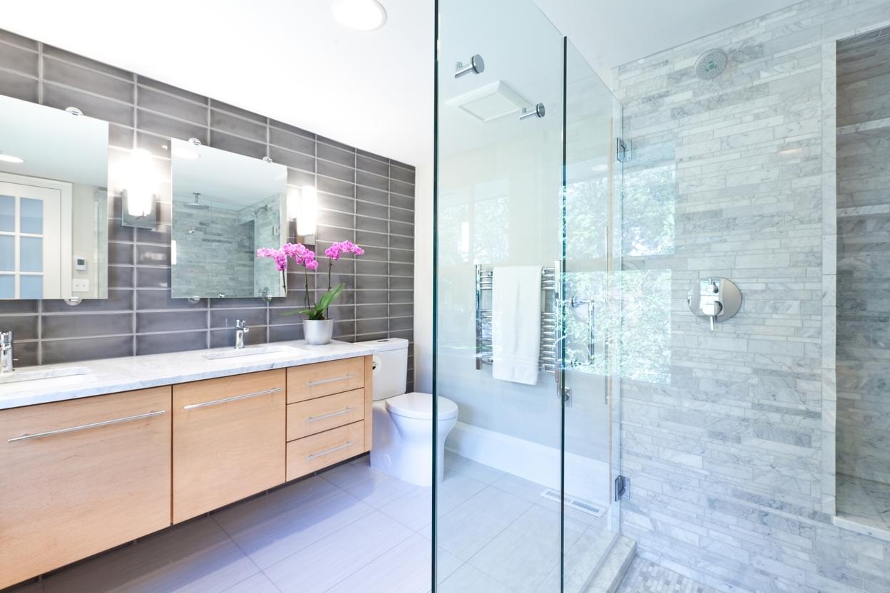 Badimpression mit offener Dusche, verschiedenem Fliesenstil in grau und hellem Holzunterschrank am weißen Waschtisch